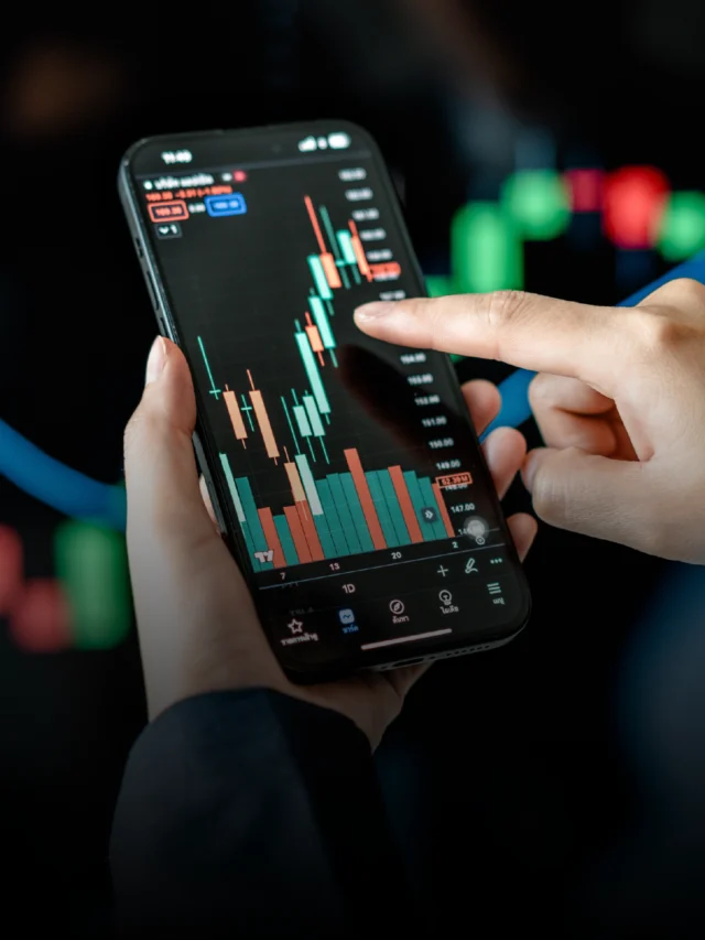 Hands holding smartphone displaying candlestick stock chart with green/red bars and price labels; alt accurately describes the visual content.